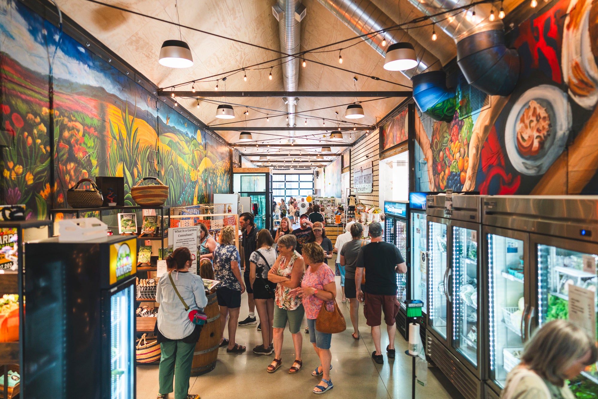 People shopping in a grocery store with colorful murals on the walls.