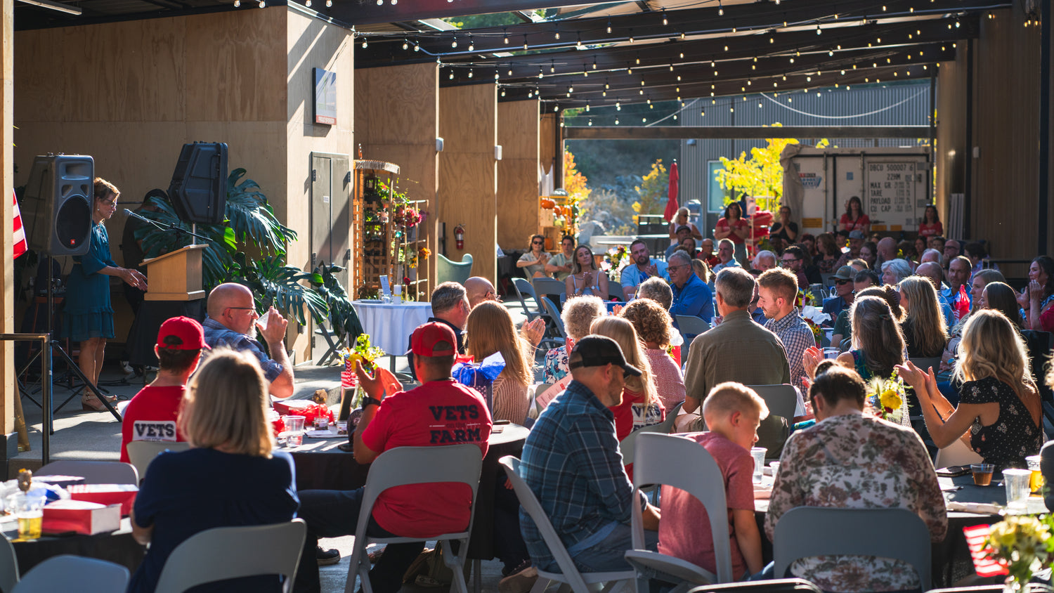 Outdoor event with people seated at tables under a covered area